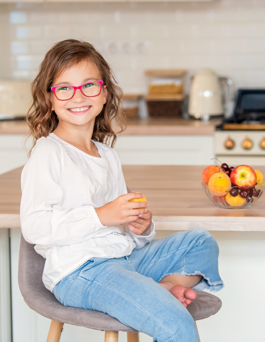 Mädchen mit pinker Brille sitzt an der Küchentheke.